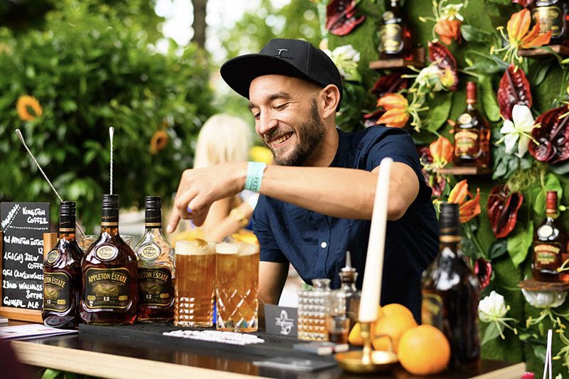 Foto eines lächelnden Barkeepers, der geschickt Cocktails auf dem Liquid Market Festival mixt und die lebhafte und qualifizierte Atmosphäre des Events verkörpert.