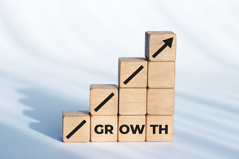 Holzblöcke, die in einer diagonalen Linie angeordnet sind und 'Wachstum' buchstabieren, symbolisieren die Entwicklung und Expansion eines Unternehmens oder einer Marke.